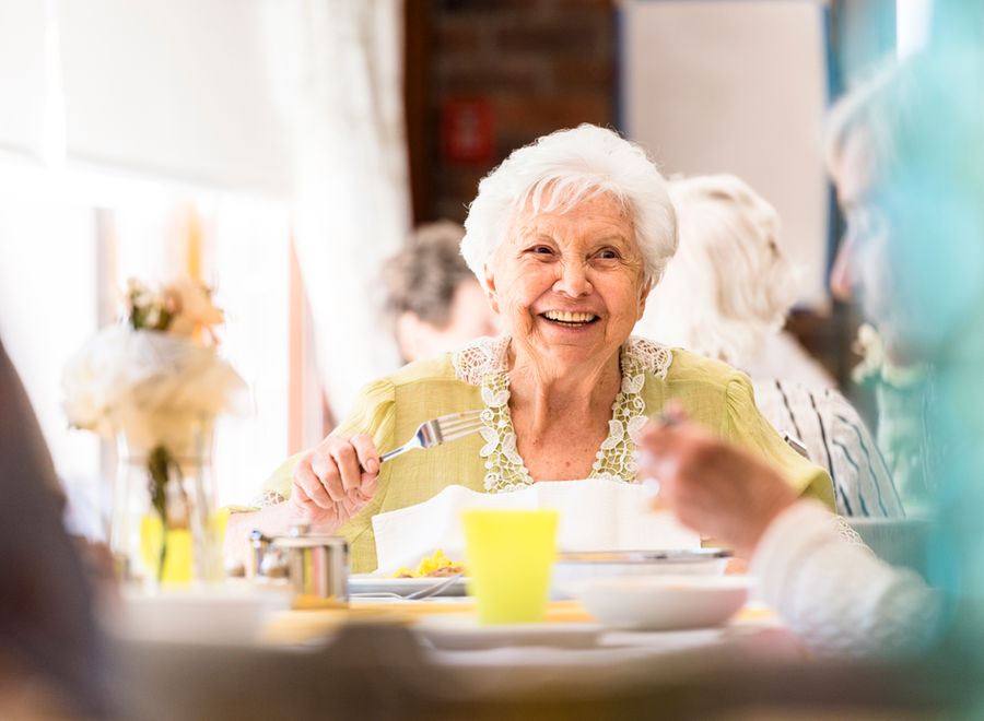 A smiling older woman having lunch at a sunlit table with friends