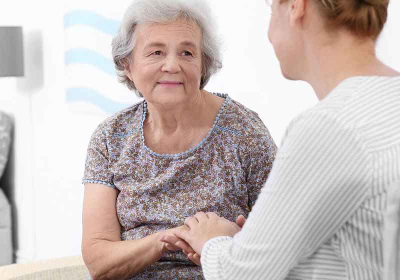 A caregiver gently holding an older woman’s hands